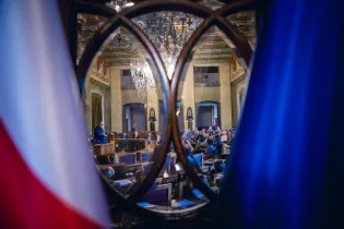 Widok na salę obrad z flagami w tle i mówcą na podium.