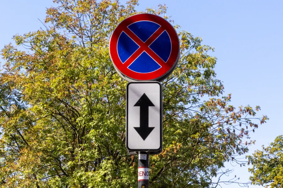 Znak drogowy zakazu parkowania z dodatkowymi informacjami o kierunku.