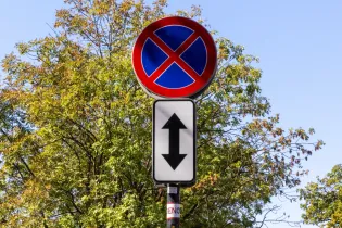 Znak drogowy zakazu parkowania z dodatkowymi informacjami o kierunku.