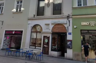 Kamienica z detalami architektonicznymi, witryna sklepu i stoliki na zewnątrz.