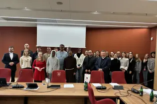 Grupa ludzi w sali konferencyjnej, uśmiechnięci, w różnorodnych strojach.